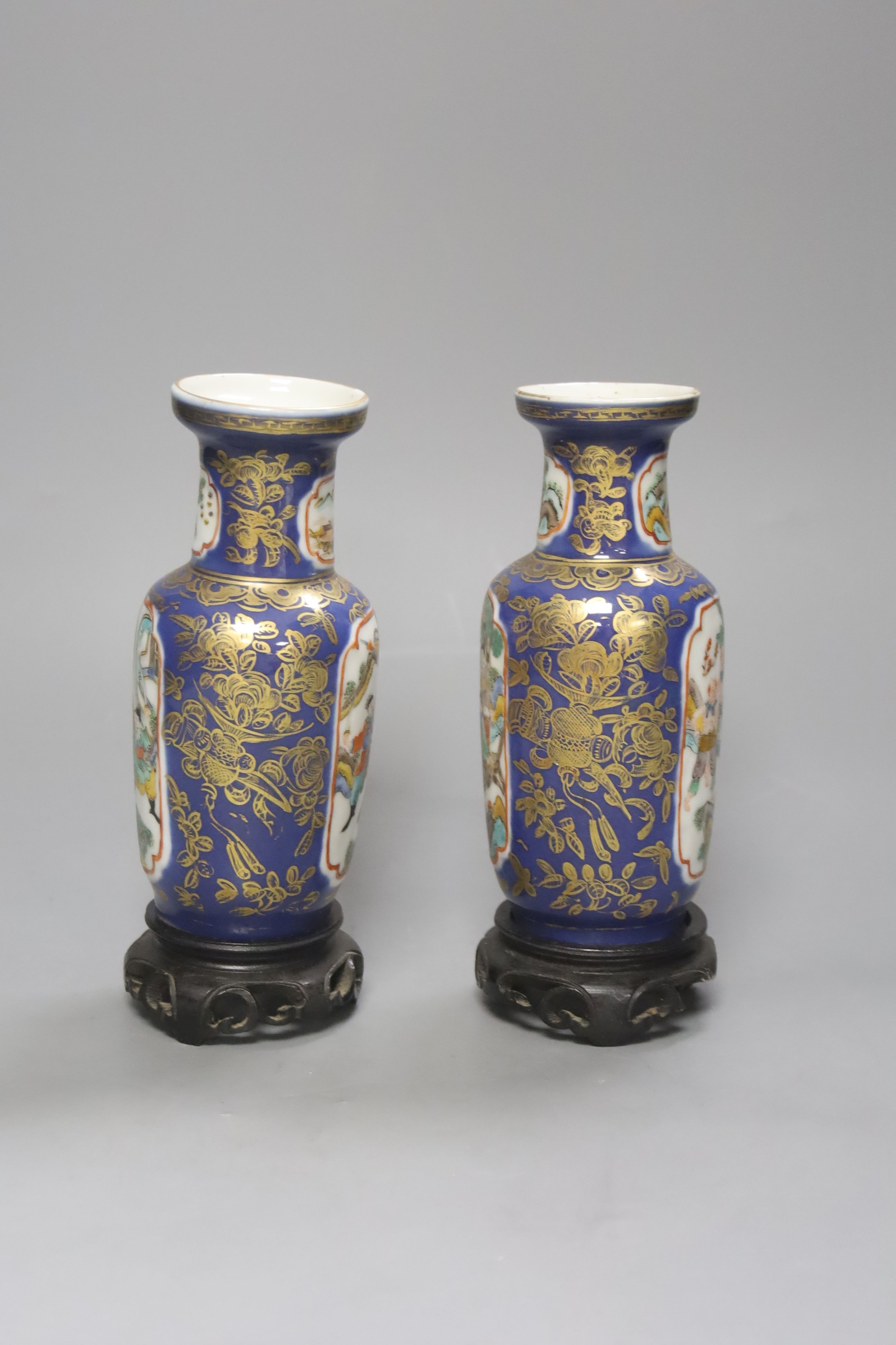 A pair of Chinese Kangxi style blue-ground vases, late 19th century decorated with panels of warriors and heightened in gilt, on carved hardwood stands, height 18cm excluding stand